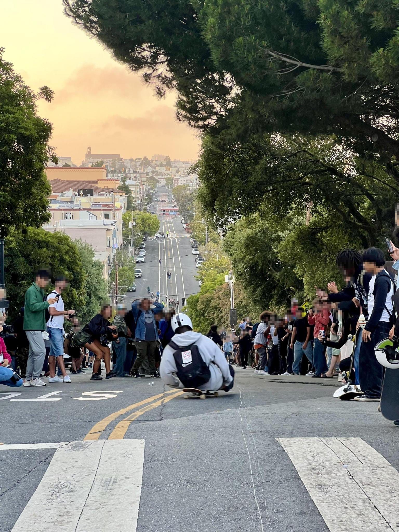 Skaters bomb down Church Street adjacent to Dolores Park as crowds watch and the sun sets in the background