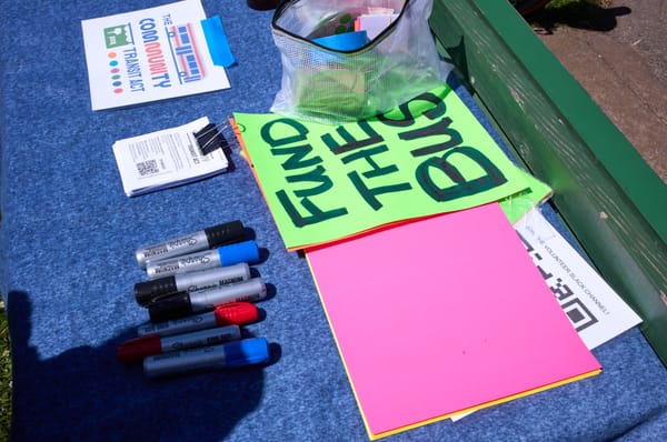 A table with sharpies, flyers, buttons, and a poster that reads "FUND THE BUS"